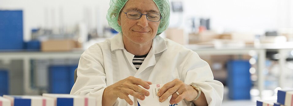 Foto: Ein Mitarbeiter im weißen Kittel hat eine Medikamentenpackung in der Hand