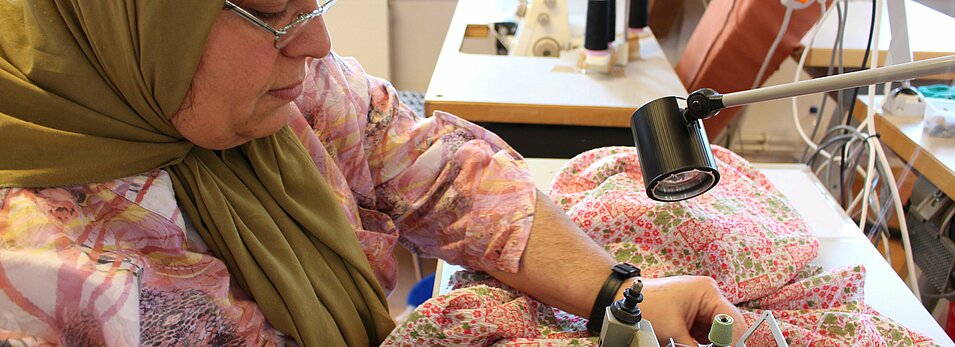 Foto: Eine Mitarbeiterin näht Stoff mit einer Nähmaschine