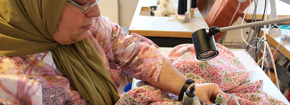 Foto: Eine Mitarbeiterin näht Stoff mit einer Nähmaschine